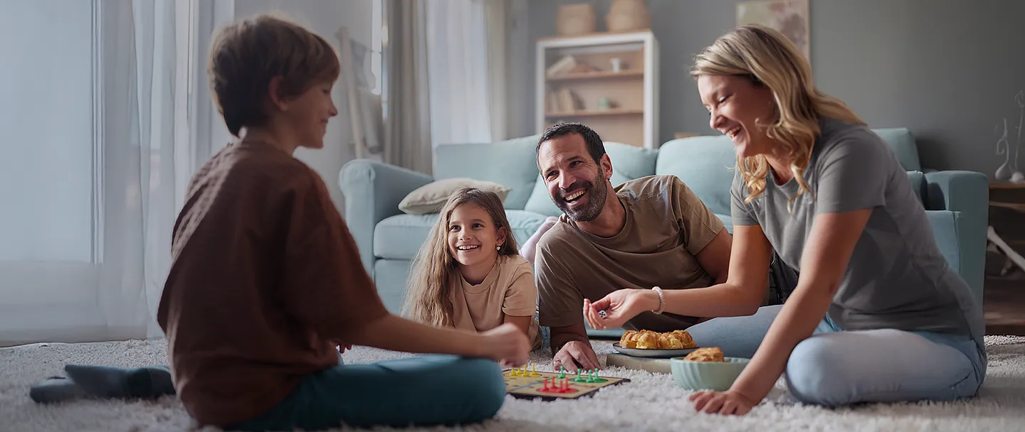 Glückliche Eltern und ihre Kinder, die zu Hause Ludo auf Teppich spielen.