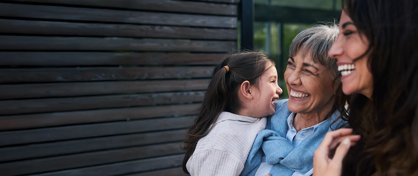 Lachendes kleines Mädchen, das mit ihrer Großmutter und ihrer Mutter draußen steht.